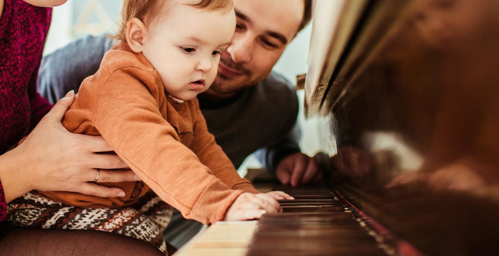 baby with hands on a piano keyboard while being held by parents