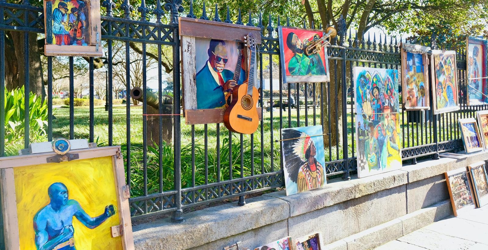 variety of artwork being sold on a fence by the park